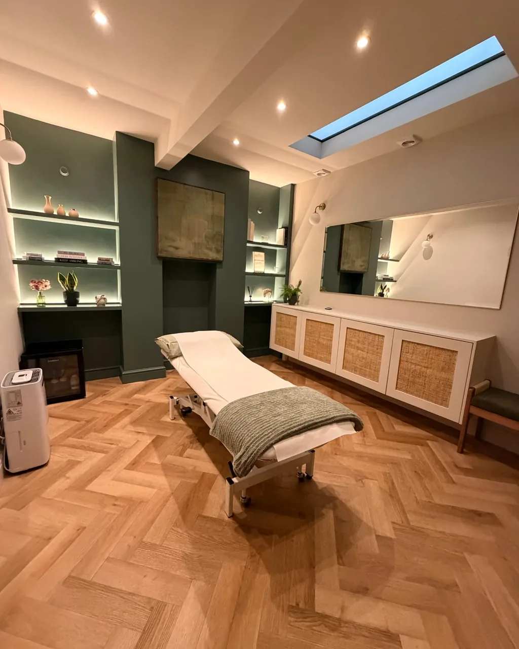 The FORMe Health physiotherapy treatment room with a treatment couch, green alcove shelving and herringbone oak flooring